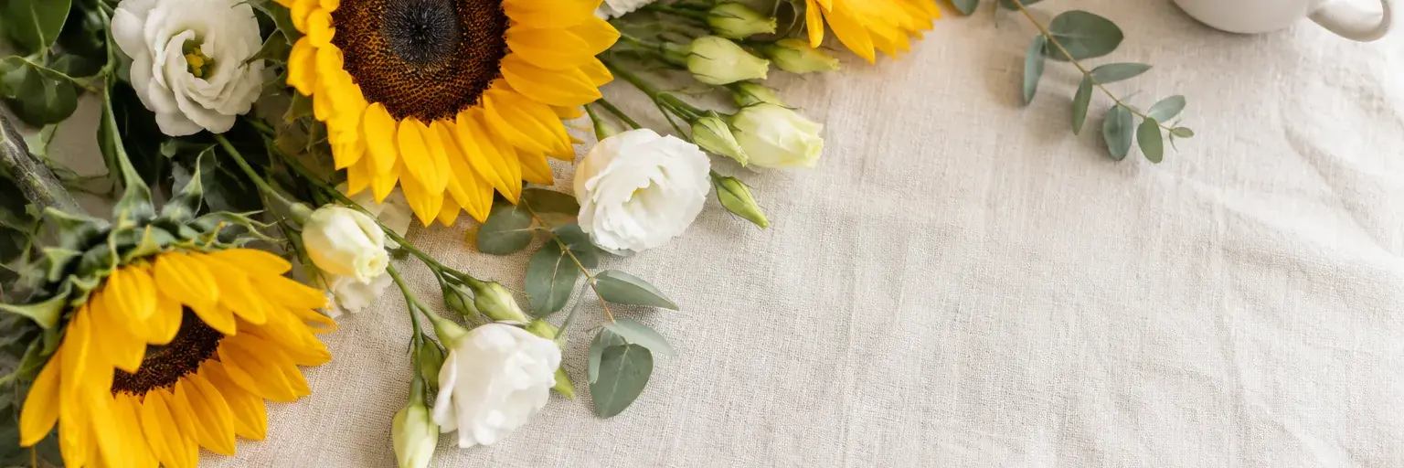 Gelbe Sonnenblumen und weiße Lisianthus neben einem schlichten Kaffeebecher.