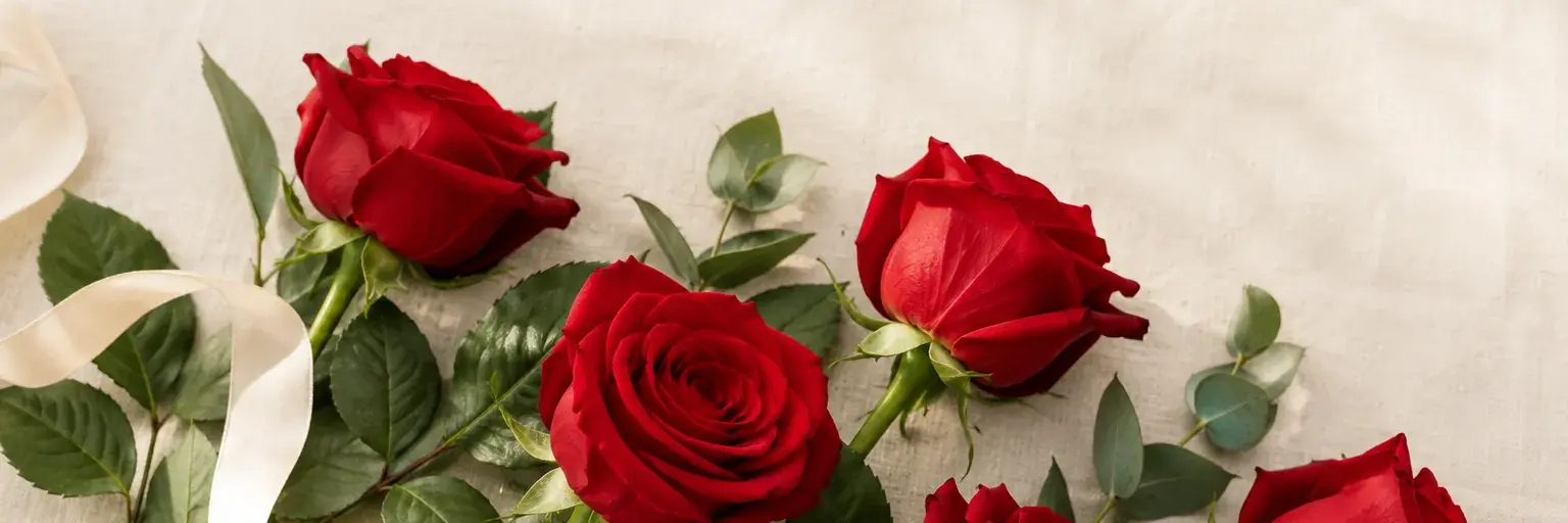 Rote Rosen mit grünen Blättern und einem elfenbeinfarbenen Band auf Leinen.