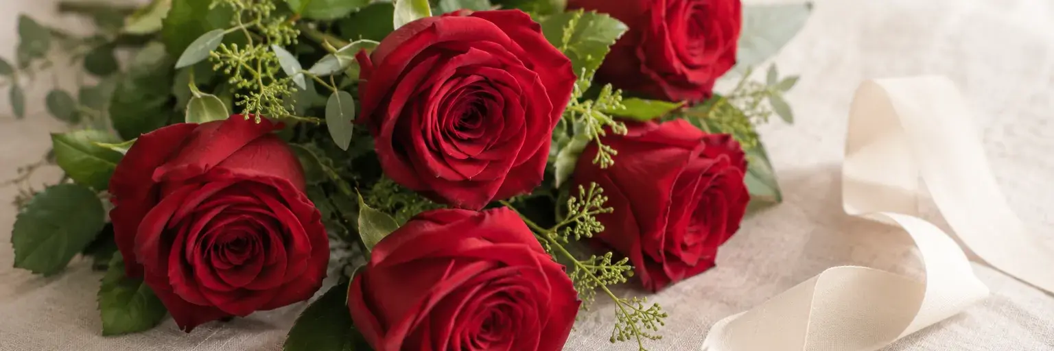 Rote Rosen mit grünen Blättern und einem elfenbeinfarbenen Band auf Leinen.