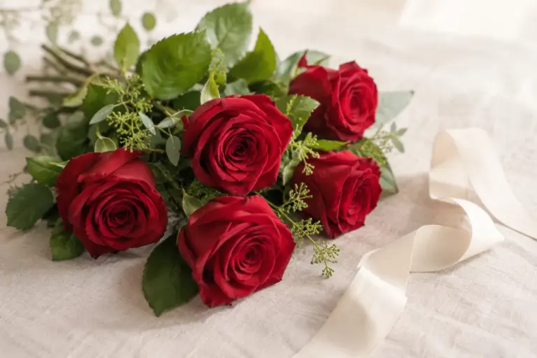 Rote Rosen mit grünen Blättern und einem elfenbeinfarbenen Band auf Leinen.
