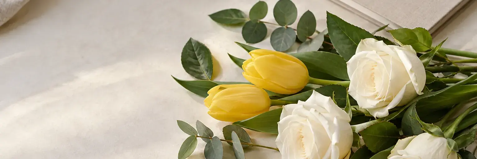 Weiße Rosen und gelbe Tulpen neben einem geschlossenen Notizbuch.