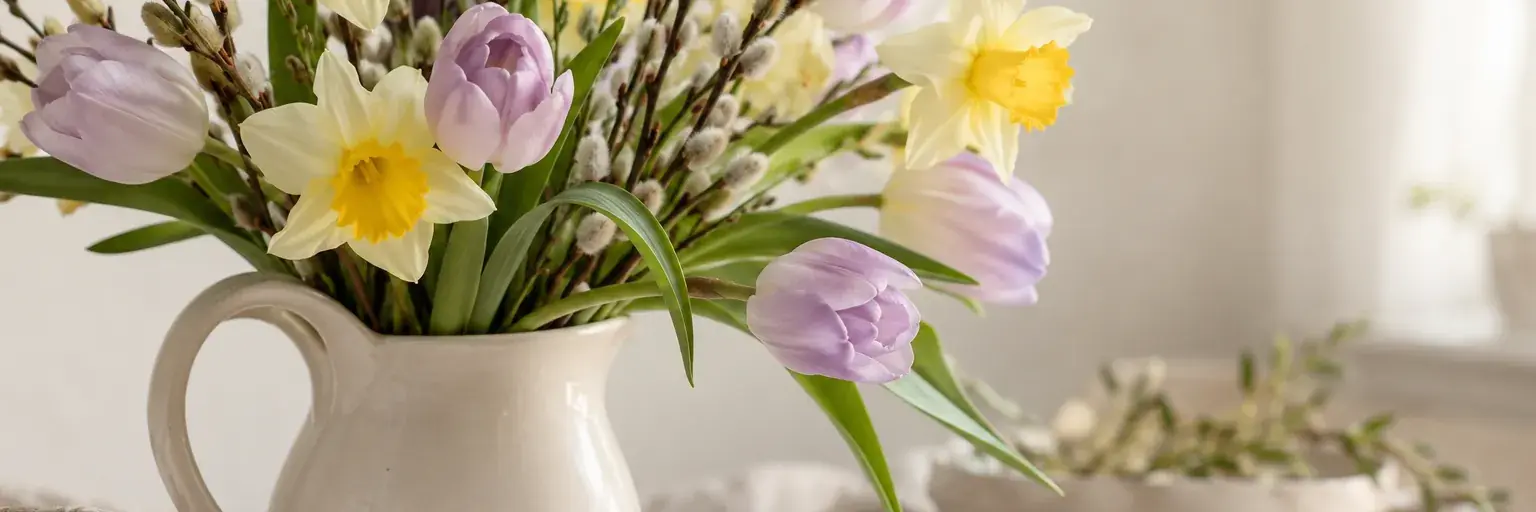 Pastellgelbe Narzissen und zartlila Tulpen mit Weidenzweigen.