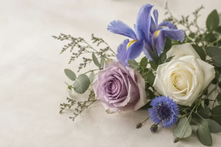 Lavendelfarbene und weiße Rosen neben einer blauen Iris und Kornblumen.