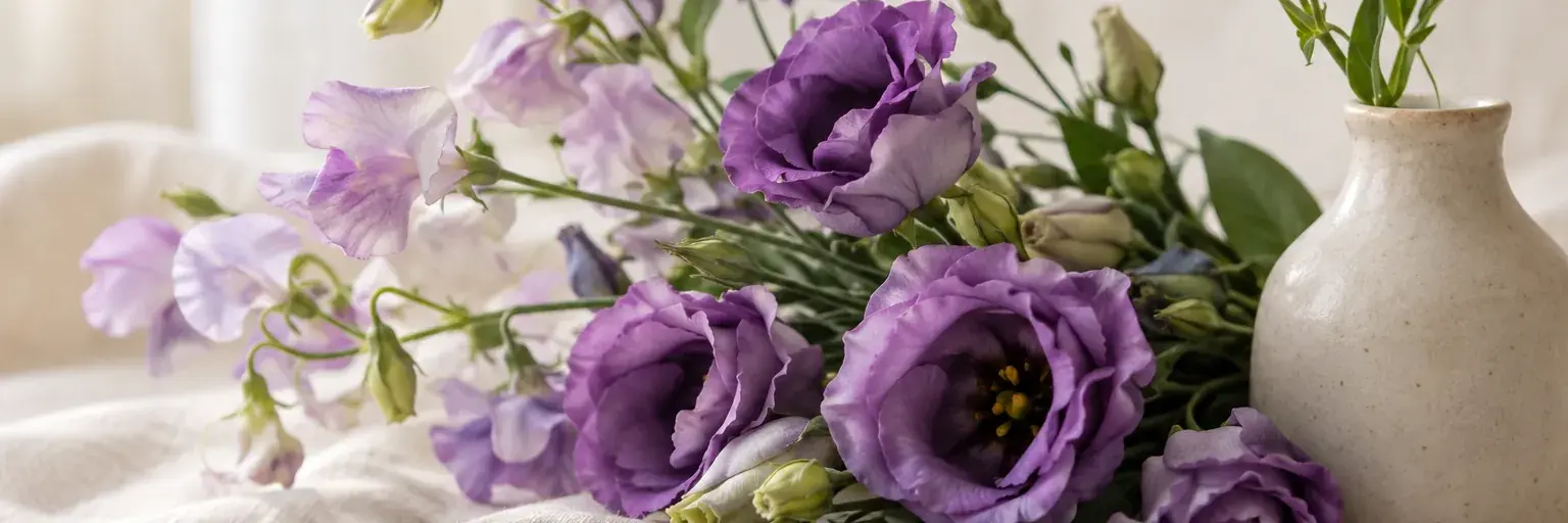 Violette Lisianthus und Duftwicken neben einer kleinen Keramikvase.