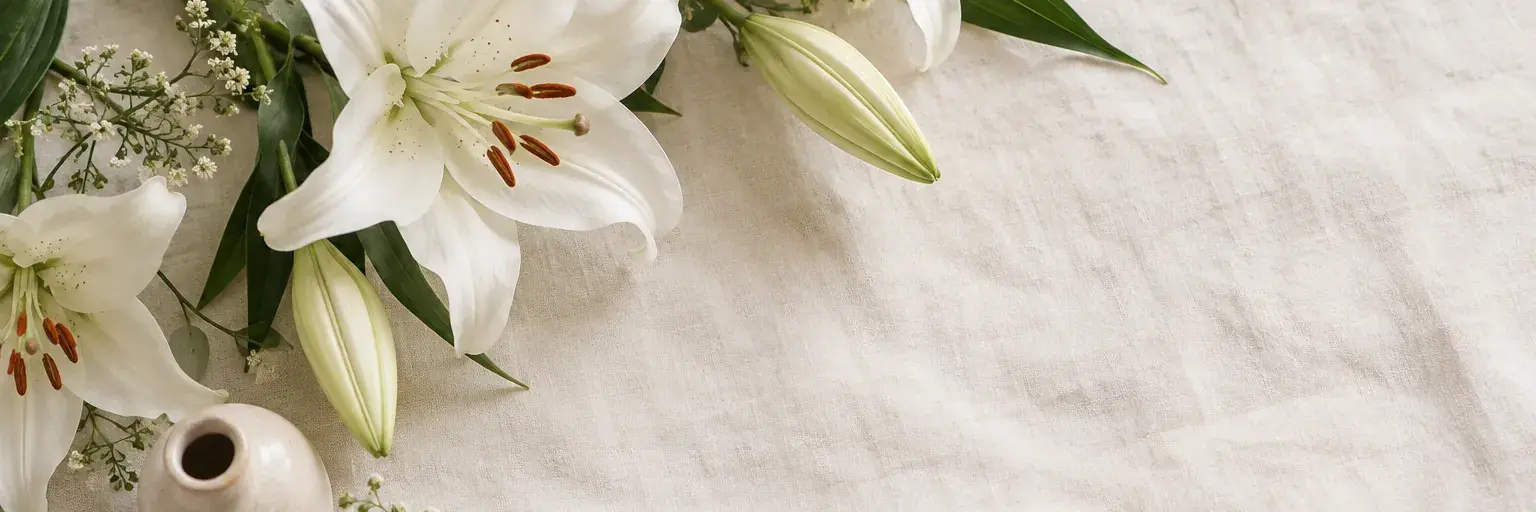 Weiße Lilien neben einer kleinen Keramikvase.