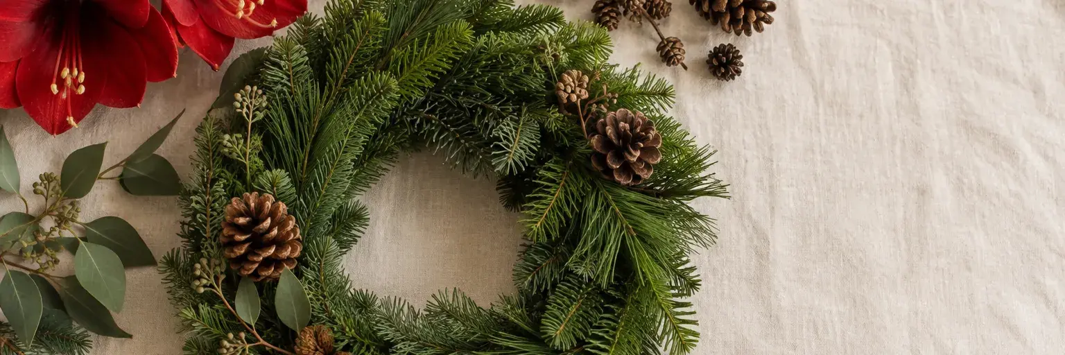 Adventskranz aus Tannen- und Kiefernzweigen mit roten Amaryllis und Zapfen.