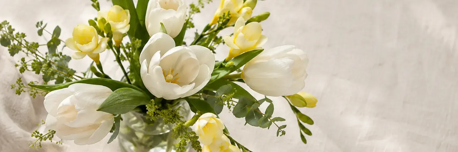 Weiße Tulpen und hellgelbe Freesien in einer kleinen Glasvase.
