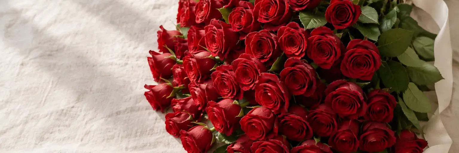 Rote Rosen mit grünen Blättern und einem elfenbeinfarbenen Band auf Leinen.