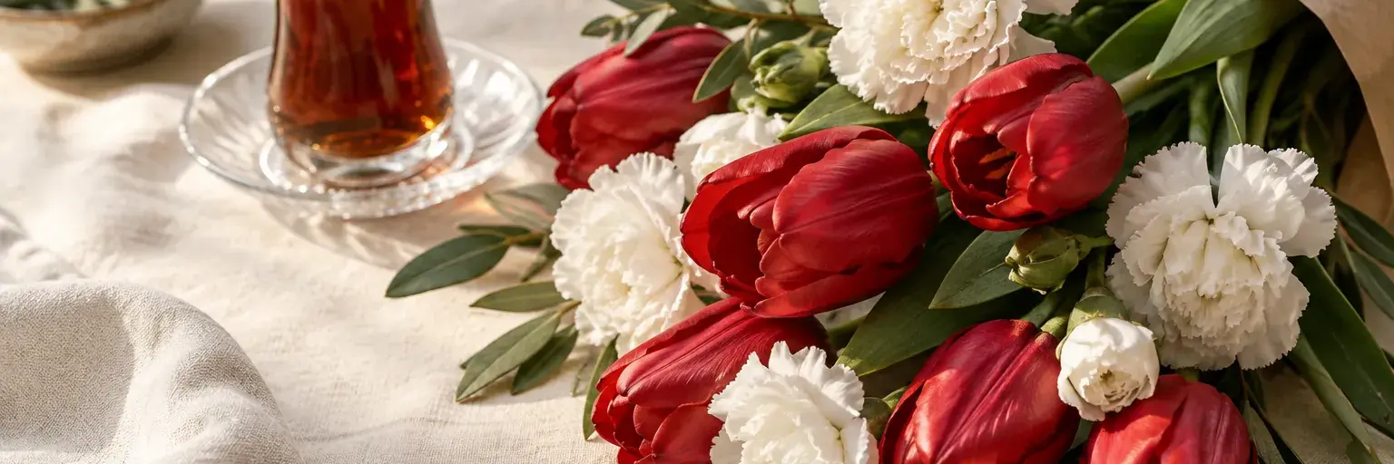 Rote Tulpen und weiße Nelken neben einem kleinen Teeglas.